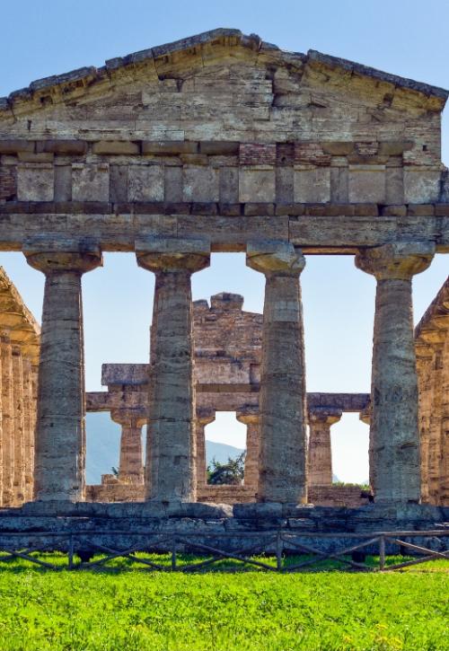 Tempio greco antico con colonne doriche, situato in un paesaggio verde e montuoso.